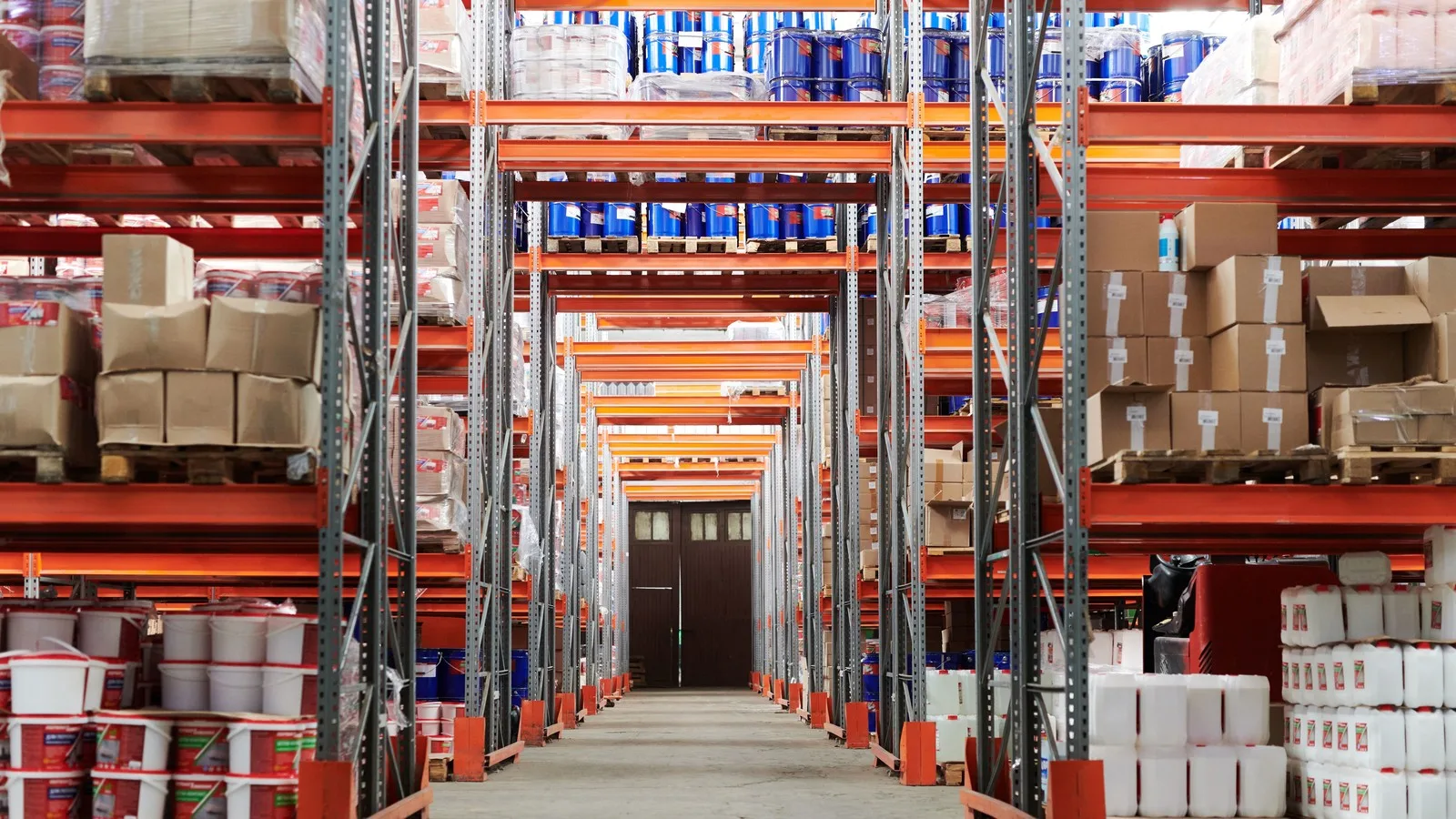 Empty warehouse aisle between tall pallet racking stacked with boxes and barrels